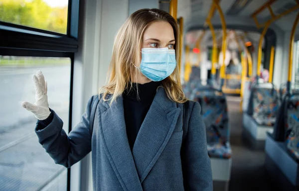 Блондинка в медичній масці і захисні рукавички стоять біля вікна в автобусі . — стокове фото