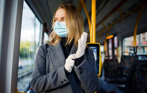 Молодая блондинка в медицинской маске и защитных перчатках, стоящая у окна автобуса . — стоковое фото