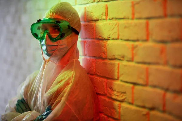 Mladý lékař v ochranném obleku a brýle na pozadí cihlové zdi v červené zóně — Stock fotografie