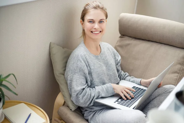 Весела блондинка дивиться в бік тримає ноутбук в руках, сидячи в кріслі — стокове фото