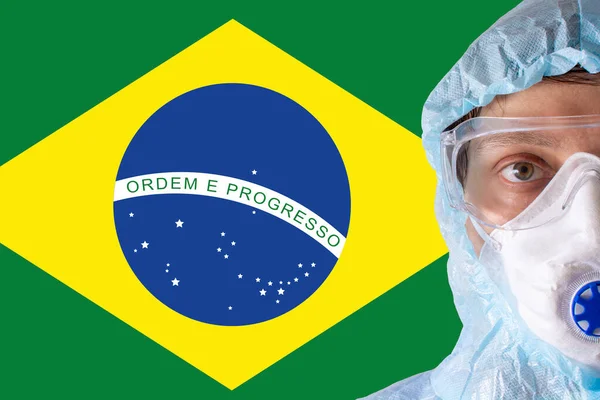 Mann in Großaufnahme in weißem Schutzanzug, Maske, Brille und Handschuhen auf dem Hintergrund der Flagge Brasiliens, der Bedrohung durch die Coronavirus-Pandemie. Epidemie, Pandemie des Coronavirus covid-19. Arzt unter Atemschutz. — Stockfoto