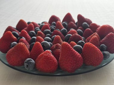 Güneş ışığının altındaki bir masada, bir kasede taze çileklerin yakın çekimi.