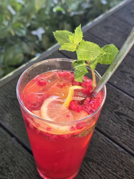 Bir bardak nane yapraklı ve ahşap masadaki buzlu kokteyl.