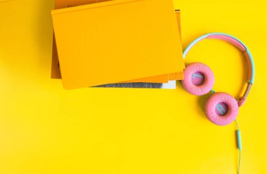 Sarı arka planda kitap ve kulaklık yığını. Audiobook konsepti. Dersleri dinle...