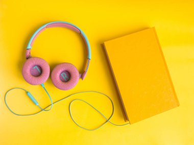Sarı arka planda kitap ve kulaklık yığını. Audiobook konsepti. Dersleri dinle...