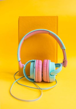 Sarı arka planda kitap ve kulaklık yığını. Audiobook konsepti. Dersleri dinle...