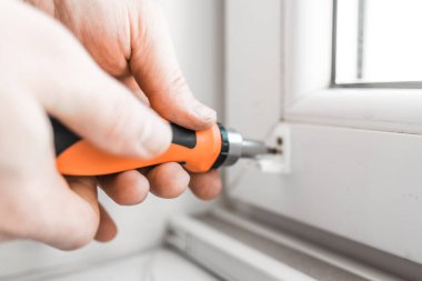 Man installs gray blackout roller blinds on window indoors, closeup.