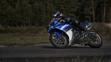 Süper spor motosikletini süren siyahlı yakışıklı motosikletçi.