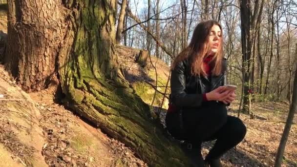 Женщина, потерявшаяся в лесу, сидит рядом с деревом и ищет сигнал на мобильном телефоне — стоковое видео