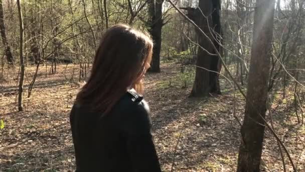 A lány fekete bőrkabát állandó az erdőben, és beszél, felháborodva nézek a távolba — Stock videók