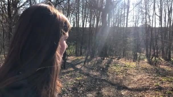 Fiatal gyönyörű kaukázusi tini lány és mosolyogva néz a kamerába, erdei úton, egy szeles napon szabadtéri portréja. — Stock videók