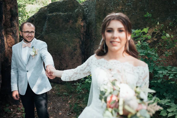 Novia y novio en el día de la boda, abrazos, de pie cerca de una roca o —  Fotos de Stock