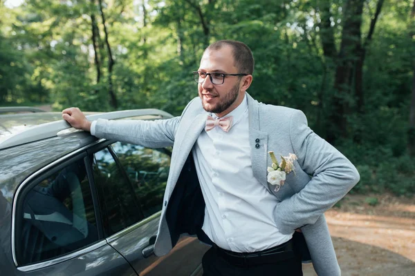 Lo sposo con la barba in una giacca grigia e occhiali sta leani — Foto Stock