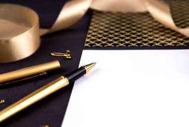 Altın kalem, kurdele, ataş ve kırtasiye siyah bir backgrou üzerinde