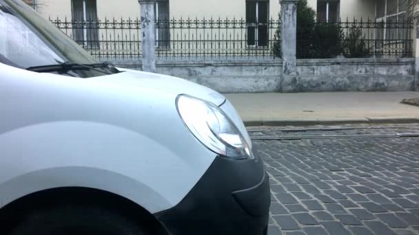 Een witte auto op een blok weg en een zwarte auto passeren door. — Stockvideo