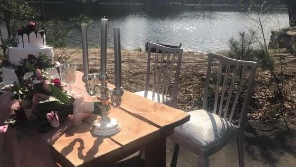 Schöner dekorativer Hochzeitstisch mit Kerzen, Blumen und einer dreischichtigen Torte weißer Farbe in der Natur — Stockvideo