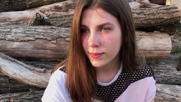 Close-up de uma menina com cabelo preto sentado em logs nos raios do sol poente . — Vídeo de Stock