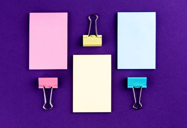 Notepad with set of colorful paper clips on purple background.bu