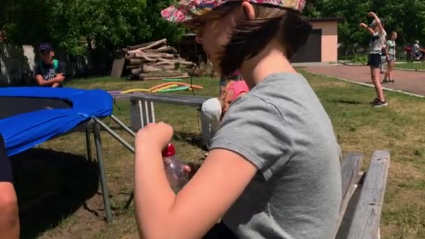 Korosten - 4. Juli 2019: Kind trinkt Wasser aus Flasche im Freien. junges Mädchen mit Wasserflasche in der Hand im Park. Junges Weibchen im Freibad genießt kaltes Wasser aus Flasche. — Stockvideo