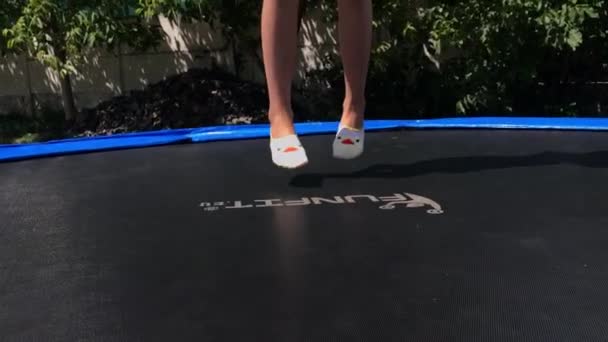 Korosten - Jule, 4, 2019: şortlu küçük kızın bacakları açık havada trambolinin üzerine atlıyor — Stok video