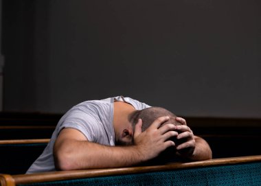 Beyaz gömlekli üzgün bir Hıristiyan adam oturuyor ve h ile dua ediyor