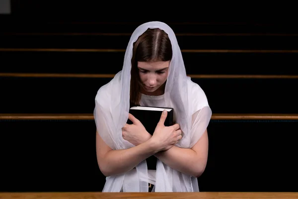 A young modest girl with a handkerchief on her head and a bible