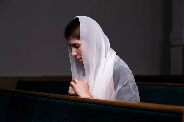 A young modest girl with a handkerchief on her head is sitting i