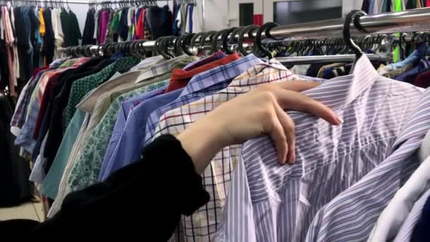 Closeup hand woman in the shop looks through jackets and shirts, which are hanging on the racks — Stock Video