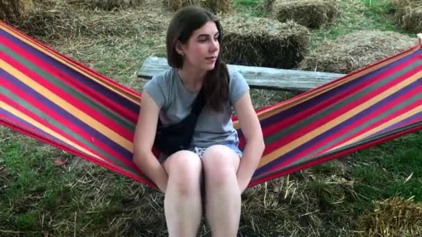 Hermosa, linda chica joven en un día de verano descansando en una hamaca de color en un parque o al aire libre — Vídeo de stock