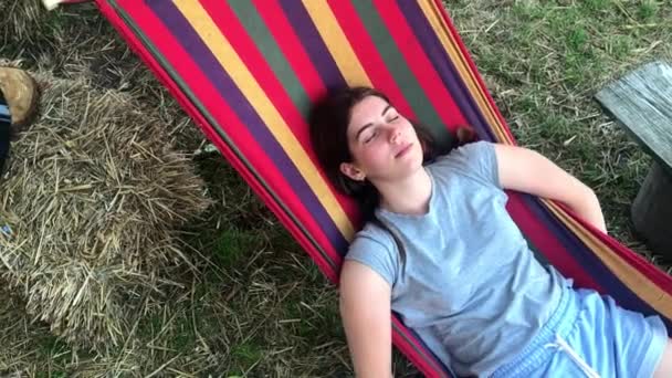 Mooi, schattig jong meisje op een zomerdag rusten op een gekleurde hangmat in een park of buitenshuis — Stockvideo