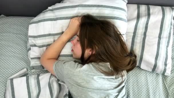 Молодая брюнетка очаровательно спит в своей постели ранним утром. Сладкий и теплый вид спокойно спящей девочки — стоковое видео