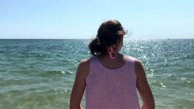 Sahilde kollarını havada, denize bakan genç beyaz bir kadının yakından bakması
