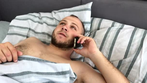 Un giovane uomo è sdraiato a letto e parlare o chiamare su uno smartphone, vista dall'alto — Video Stock