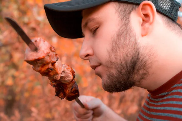 Man is eating shish kebab. Bearded man eats a shish kebab tearin — Stock Photo, Image