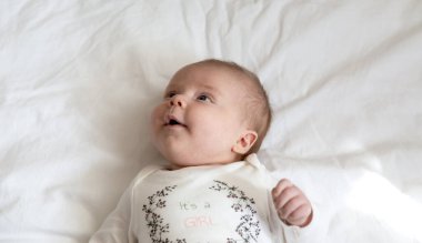 Yatakta yatıp gülümseyen bir kızın yakın plan portresi. Sarı elbiseli üç aylık kız gülüyor. Yüksek kalite fotoğraf