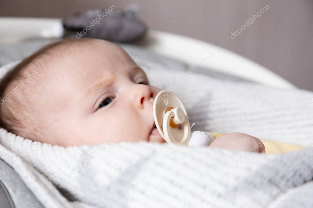 A close-up portrait of a newborn baby girl, who lies in a cradle and sucks a pacifier. . High quality photo