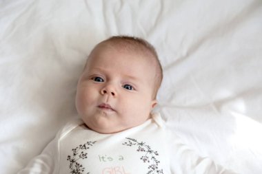 Yatakta yatan bebek kızın şaşırmış ve ciddi yüzünün yakın plan portresi. Üç yaşında bir kız.