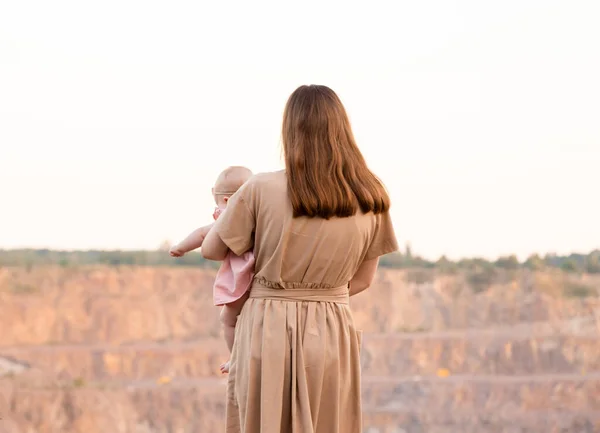 Een jonge moeder staat naar de groeve of de bergen te kijken en houdt een kind in haar armen. Zonsondergang. Close-up, zicht van achteren. Actieve levensstijl. Reizen. — Stockfoto