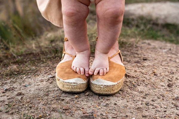 Las piernas del bebé se paran en los pies de la madre, la mamá apoya a la pequeña hija del bebé.Primeros pasos. Mamá enseña a su hijo a estar de pie y estar en equilibrio. —  Fotos de Stock