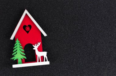 Noel düzleştirmesi düzeni. Ahşap oyuncak ev, bir geyik ve parlak siyah arka planda bir Noel ağacı. Yazmak için yeri olan Noel kartı