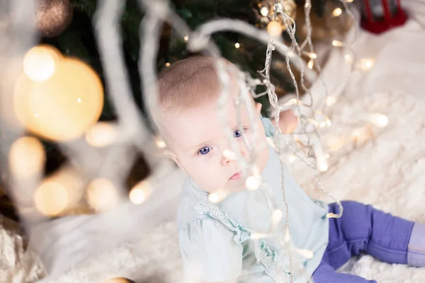 Baby Jeans Sits Christmas Tree Looks Garland Blur Foreground — Stock Photo, Image