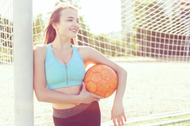 Futbol sahasında bir kadın kollarında bir futbol topu tutuyor..