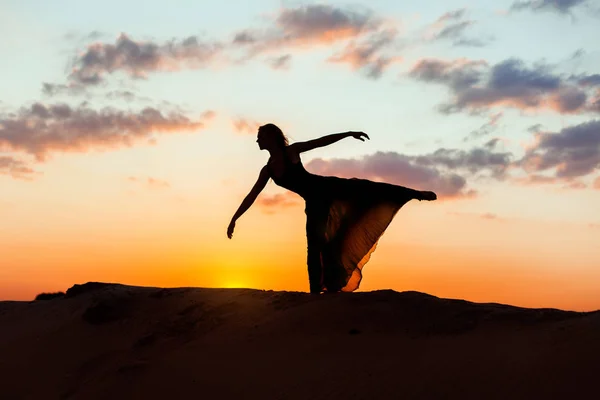 Silhouette of a young woman in the setting sun, she dances a dance.