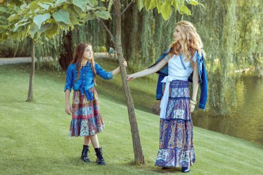 Anne ve kızı göl kenarında duruyor. Onlar bir boho tarzında giyiniyorsun.