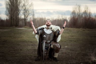 Bir zincirden giyen Knight yalvaran, gökyüzünde ellerini kaldırdı.