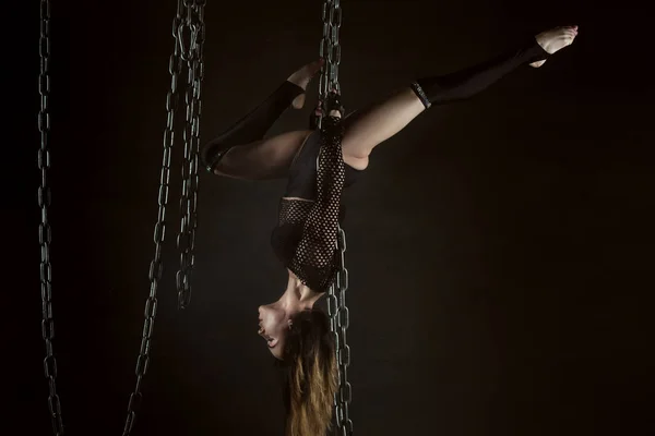 Woman gymnast hangs on chains, she shows performance.