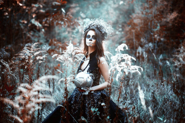Young woman with Halloween make-up in fairytale forest with pumpkin.
