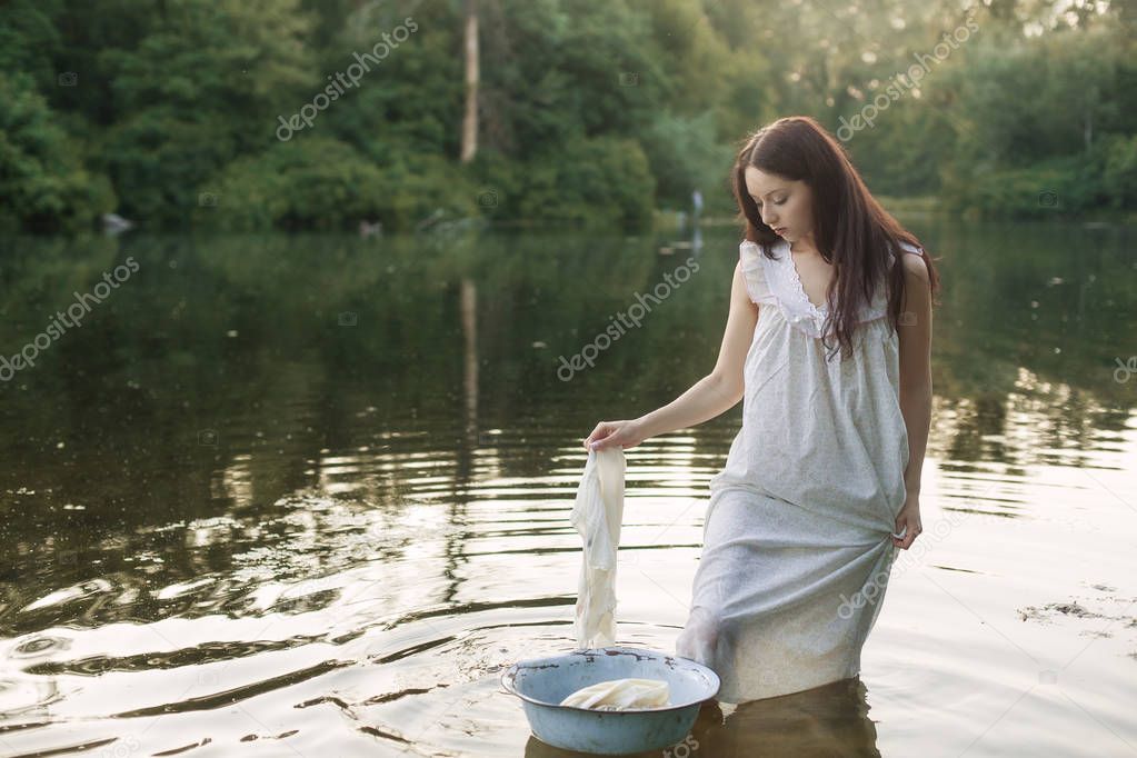 Young woman in nightie in the river washes clothes.
