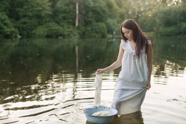 Giovane donna in camicia da notte nel fiume lava i vestiti . — Foto Stock