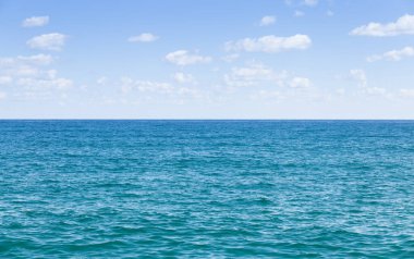 Mavi gökyüzü ve beyaz bulutlarla berrak deniz ufku.